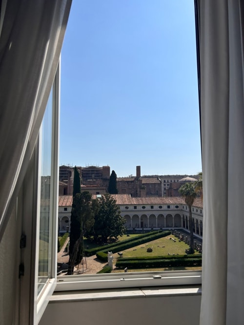 Vista dalla finestra del giardino del chiostro di Michelangelo presso la Michelangelo Suite Roma, con siepi curate e architettura romana storica