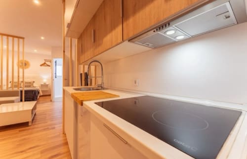 Cocina moderna de apartamento en Mérida con estufa de inducción, gabinetes de madera y sala de estar abierta