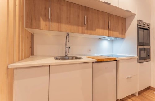 Cocina moderna en apartamento de Mérida con gabinetes de madera, encimeras blancas, fregadero de acero inoxidable y electrodomésticos empotrados