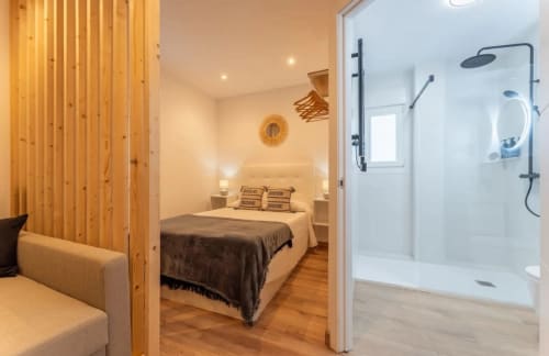 Dormitorio moderno con baño privado y ducha en apartamento de Mérida, con divisor de madera y vistas a la ciudad