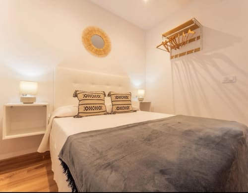 Dormitorio moderno en apartamento de Mérida con vistas a la ciudad, cabecera en crema, almohadas geométricas y detalles en madera natural