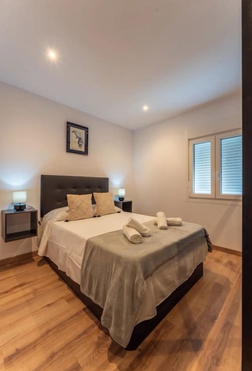 Moderno dormitorio en apartamento Gestyp-AT de Mérida con cama queen, cabecero oscuro, pisos de madera y vistas a la ciudad