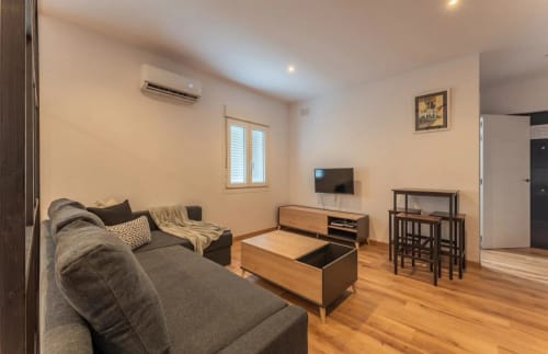 Moderna sala de estar en Mérida con sofá gris, muebles de madera, TV y zona de comedor