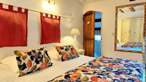 Chambre de la Suite Bergerie à La Bergerie Du Moulin, Taradeau. Lit queen-size avec parure florale colorée, rideaux rouges, décor bois