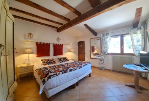 Suite chambre spacieuse à La Bergerie Du Moulin avec poutres apparentes, literie colorée, lampes jumelées et rideaux tropicaux