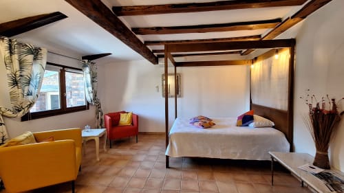 Chambre spacieuse de la Suite Sheepfold à La Bergerie Du Moulin avec lit à baldaquin, coin salon, poutres apparentes et carrelage en terre cuite