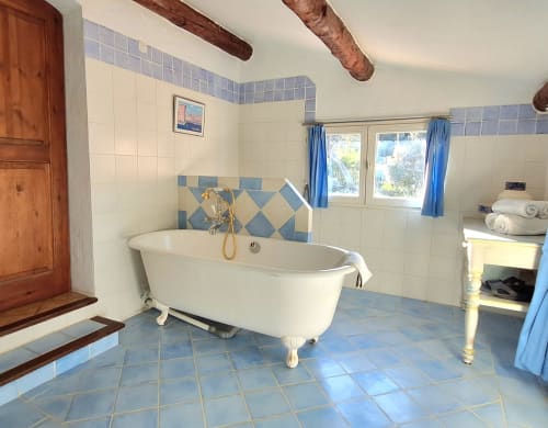 Lavender room bathroom at La Bergerie Du Moulin featuring a clawfoot bathtub with blue tile accents and natural light from