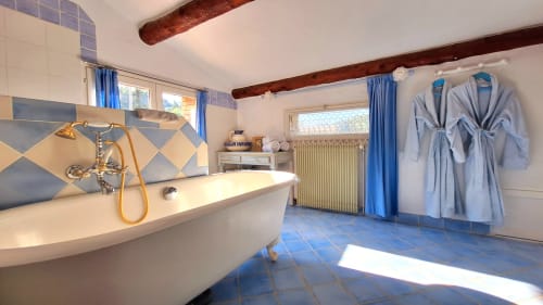 Spacious bathroom with white bathtub, gold fixtures, blue tile floor, and robes at La Bergerie Du Moulin in Taradeau