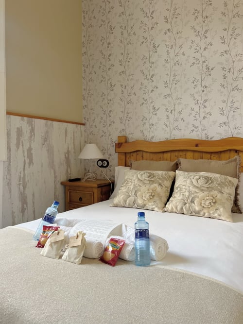 Cozy bedroom at La Venta de Miyares with wooden bed, floral wallpaper, welcome amenities, and water bottles on bed.