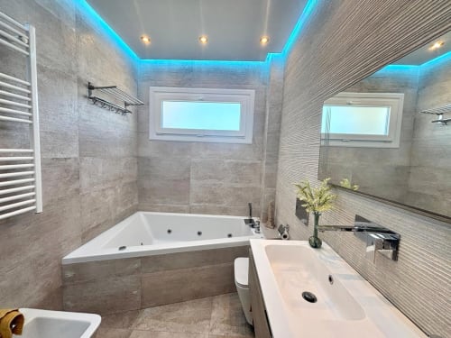 Baño moderno con bañera spa, ducha de efecto lluvia y techo iluminado en la casa Holibai, Baiona