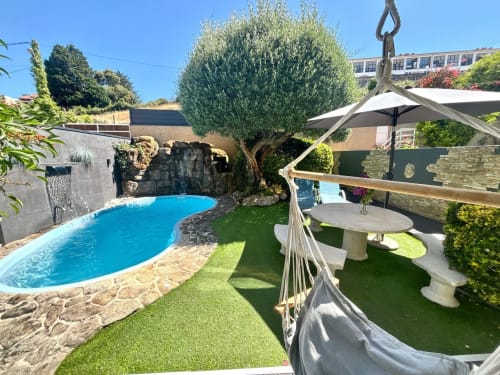 Jardín privado  en Baiona con piscina azul, olivo, hamaca y zona de descanso bajo sombrilla.