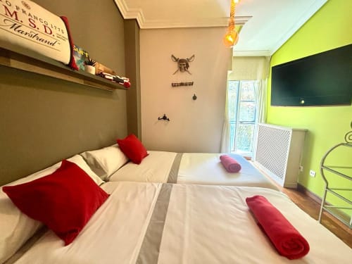 Dormitorio moderno en la casa Serenidade de Holibai de Baiona con camas gemelas, almohadas rojas, pared de acento verde lima y balcón con vistas al mar.