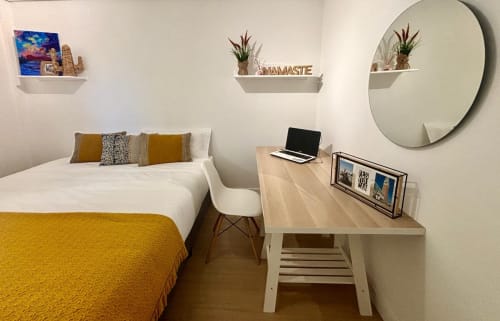 Dormitorio moderno en la casa  Holibai de Baiona con cama, escritorio, espejo redondo y estantes decorativos