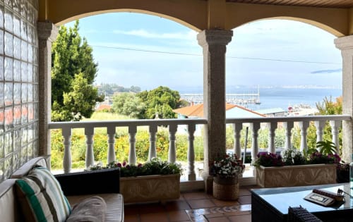 Vista desde la terraza de Serenidade: balcón costero de Baiona con mar, embarcaciones y jardines exuberantes
