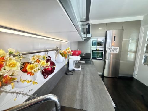Cocina moderna en la Serenidade, Baiona, con electrodomésticos de acero inoxidable, encimeras oscuras, flores frescas y diseño contemporáneo