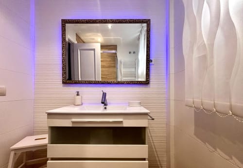 Baño moderno de la casa Serenidade con espejo iluminado, tocador blanco y amenidades de spa en Holibai, Baiona