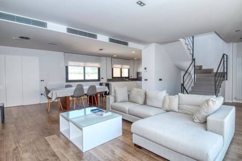 Modern duplex apartment in Calella with open-plan living area, white L-shaped sofa, dining table, and staircase to upper