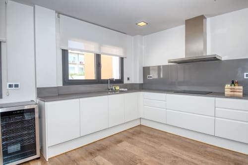 Modern white kitchen with gray countertops, stainless steel hood, and wooden floors in Calella apartment