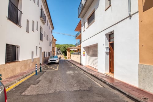 Narrow residential street in Palafrugell with white apartment buildings, parked car, and clear blue sky