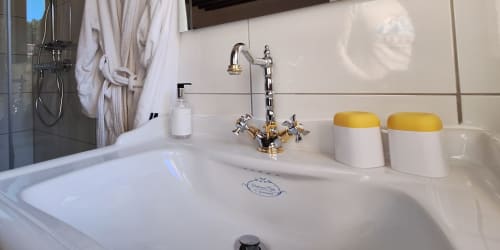 Lavabo de la salle de bains à La Bergerie Du Moulin avec plan de travail blanc, robinetterie dorée et distributeurs de savon jaunes à Taradeau