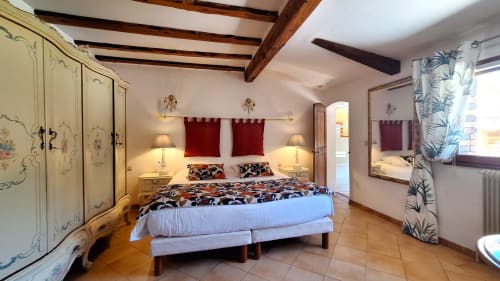 La chambre de la Suite de la Bergerie à La Bergerie Du Moulin, Taradeau avec lit queen-size, armoire ornementée, poutres apparentes et élégante