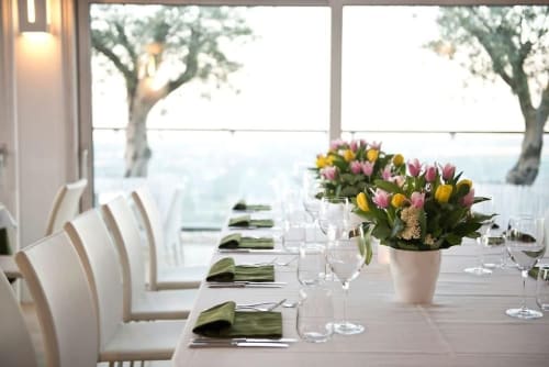 Elegant dining room at Al Mirador Resort in Fasano with panoramic lake views, white chairs, and colorful tulip centerpieces
