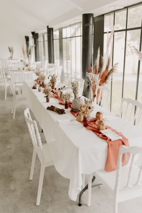 Élégante réception de mariage au Château de Baylac avec nappes blanches, chemins de table corail et centres de table en fleurs séchées