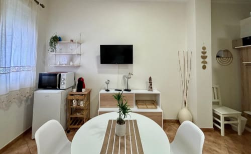 Moderno estudio en Baiona con mesa de comedor redonda blanca, cocineta, TV en pared y decoración minimalista