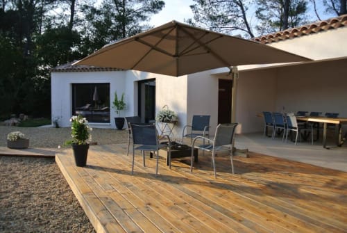 Patio du Carpe Diem Résidence hôtel à Lorgues avec terrasse en bois, parasol, salon extérieur et bâtiment blanc