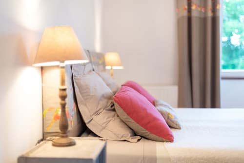 Cozy bedroom at L' Amiradou B&B in Félines-sur-Rimandoule with pink pillow, beige bedding, and warm bedside lamp.