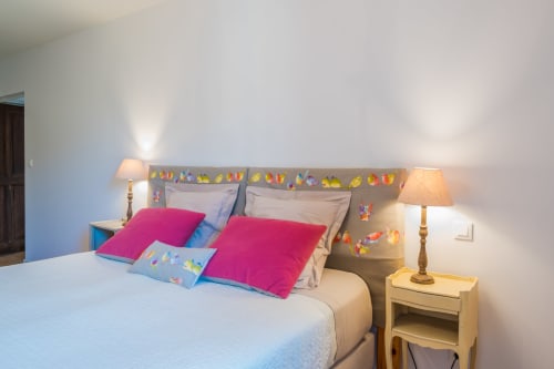 Cozy bedroom at L'Amiradou B&B with colorful bird decor, pink pillows, and warm bedside lamps