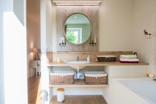Modern bathroom at L'Amiradou B&B in Félines-sur-Rimandoule with round mirror, wooden vanity, and wicker storage baskets