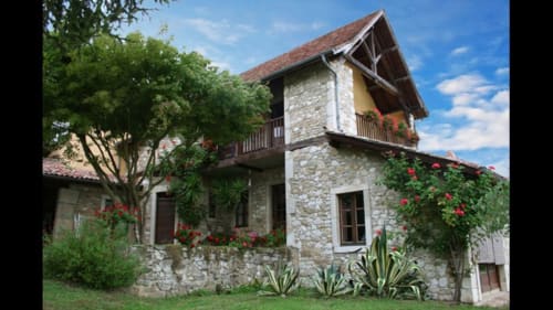 Château de Baylac, maison en pierre avec fleurs rouges, balcon en bois et jardins luxuriants à Bugnein, France