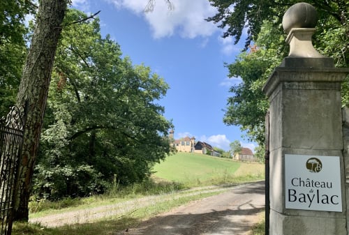 Entrée du Château de Baylac avec pilier en pierre, allée bordée d'arbres et manor sur colline à Bugnein, France