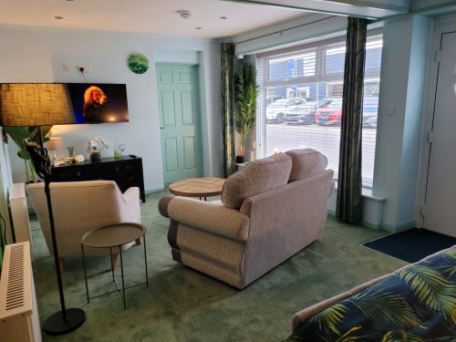 Modern apartment sitting area with upholstered armchair, side table, and flat-screen TV at Jane's B&B in Guisborough, GB