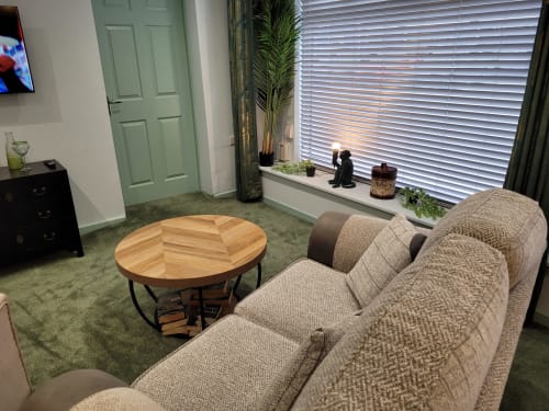 Cozy sitting area in Jane's B&B apartment with beige sofa, round wooden coffee table, green door, and window with blinds in