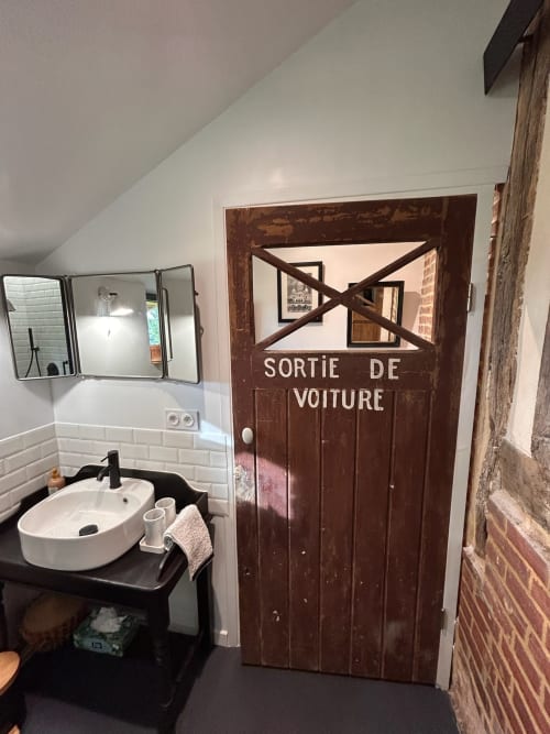 Salle de bains à Domaine de Blanvatel avec carrelage subway blanc, lavabo rond et porte en bois vintage marquée 'Sortie de Voiture'