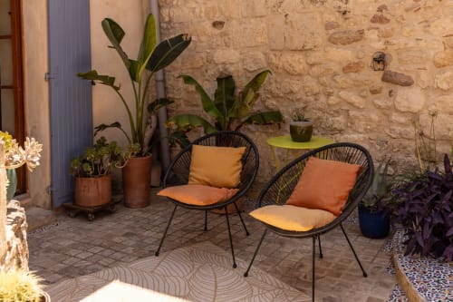 Coin détente douillet au Prieuré Notre-Dame avec fauteuils en rotin, plantes en pot et murs en pierre brute à Montfrin