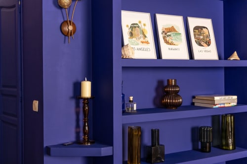 Modern blue shelving unit in Charles Suite at Le Prieuré Notre-Dame featuring vintage travel prints, brass accents, and