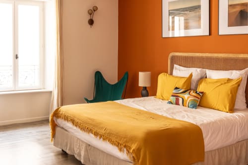 Modern bedroom at Le Prieuré Notre-Dame in Montfrin with orange accent wall, yellow bedding, rattan headboard, green