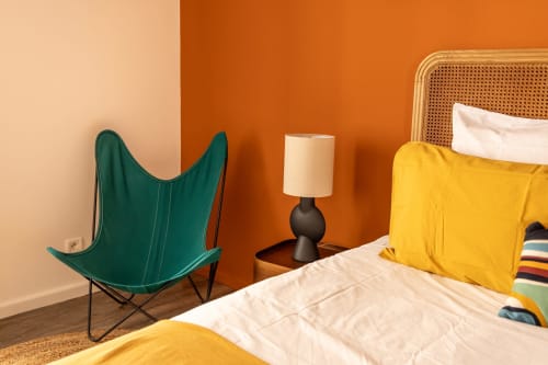 Modern bedroom at Le Prieuré Notre-Dame with green butterfly chair, orange accent wall, yellow bedding, and rattan headboard