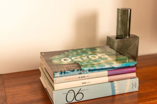 Stack of fashion and design books on wooden table with perfume bottle at Le Prieuré Notre-Dame