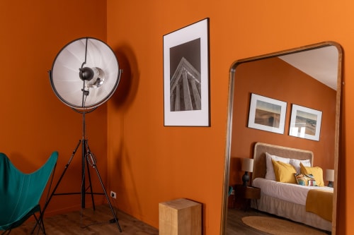 Modern Charles Suite at Le Prieuré Notre-Dame with orange walls, tripod lamp, framed artwork, and mirror reflecting bedroom