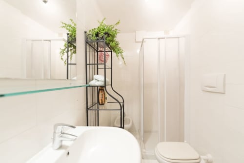 Moderno bagno dell'appartamento Le Arche a Verona con sanitari bianchi, scaffale in metallo nero e piante verdi sospese