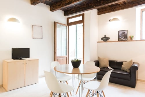 Moderno soggiorno con zona living, tavolo da pranzo, divano nero, travi in legno, TV e vista sulla città a Le Arche Verona