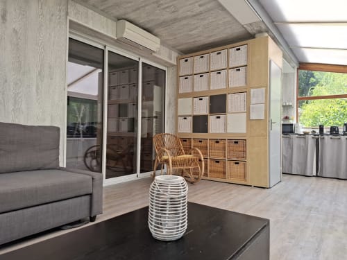 Intérieur cottage moderne à Accolade Châteaudun : canapé gris, fauteuil en rotin, meuble de rangement, portes coulissantes donnant sur la rivière