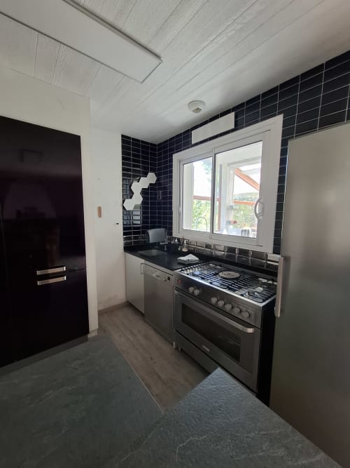 Cuisine moderne du cottage Accolade à Châteaudun avec crédence en carrelage noir, électroménagers inox et vue sur la rivière