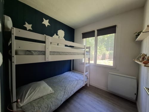 Chambre d'enfants moderne au gîte Accolade à Châteaudun avec lits superposés blancs, mur d'accent bleu marine et vue sur la rivière.