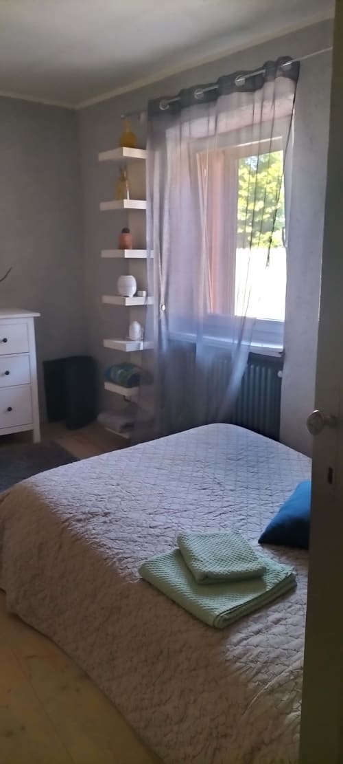 Bright bedroom with bed, floating shelves, and garden-facing window with sheer curtains at CasaRosada wellness retreat in