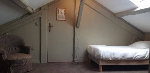 Chambre mansardée de l'hôtel Les Cabines à Houlgate avec plafonds inclinés, fauteuil, lit et porte